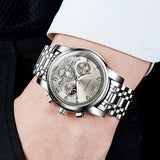 Silver wristwatch with detailed face on a person's wrist against a dark background